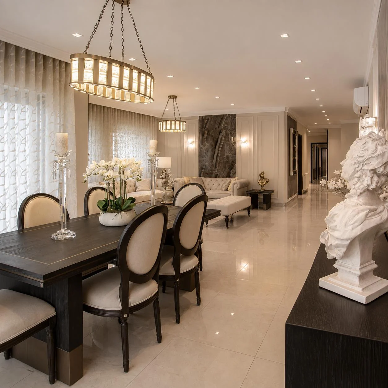 A cream living and dining space with lantern chandeliers and a classical white bust