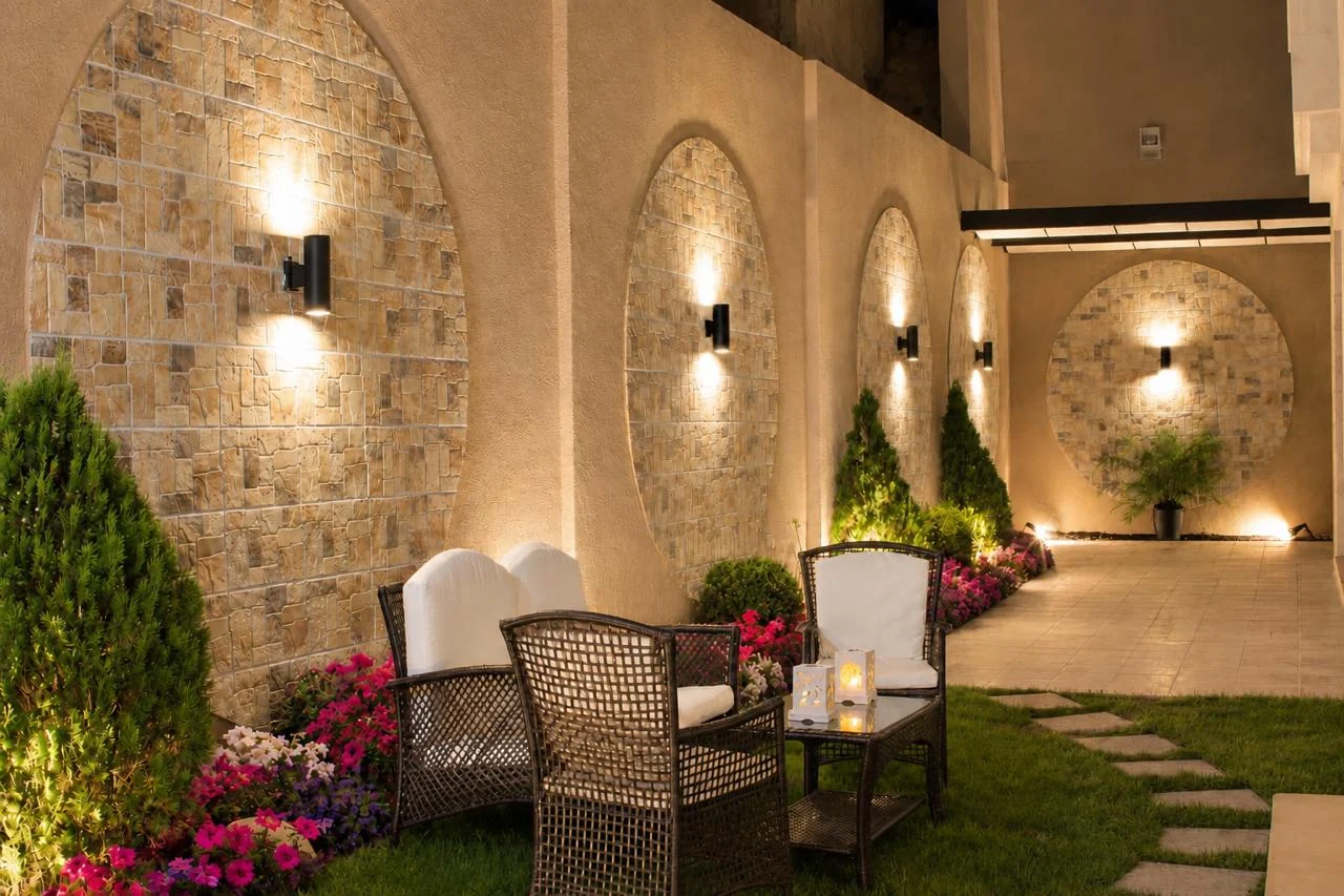 An illuminated garden seating area with circular stone wall details and colourful planting