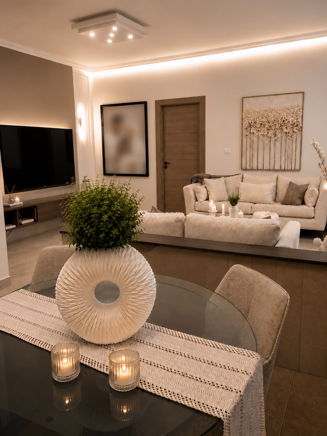 A warm family living room seen across a dining table with a sculptural white vase